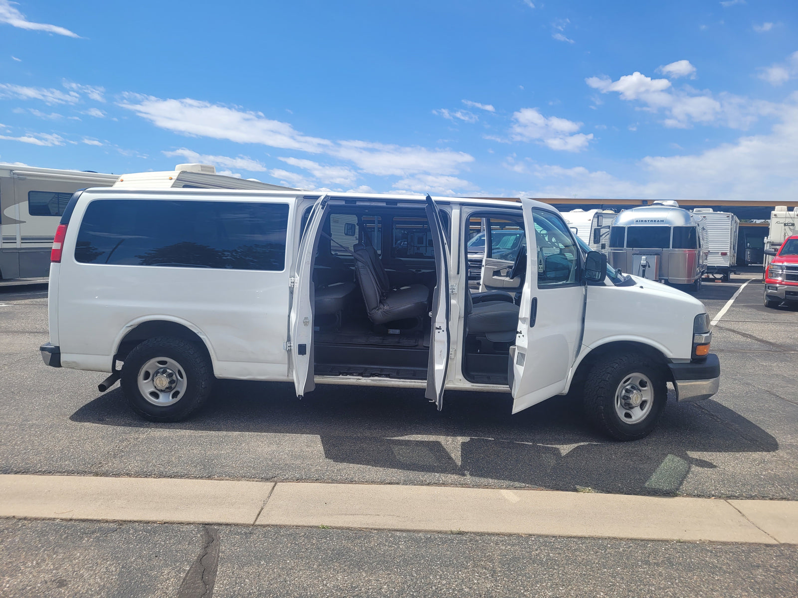 White van with open doors at an RV rental facility, amidst various RVs including an Airstream.