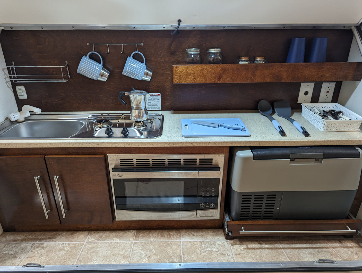 This RV rental offers a well-equipped kitchen with a sink, stove, microwave, and portable fridge.