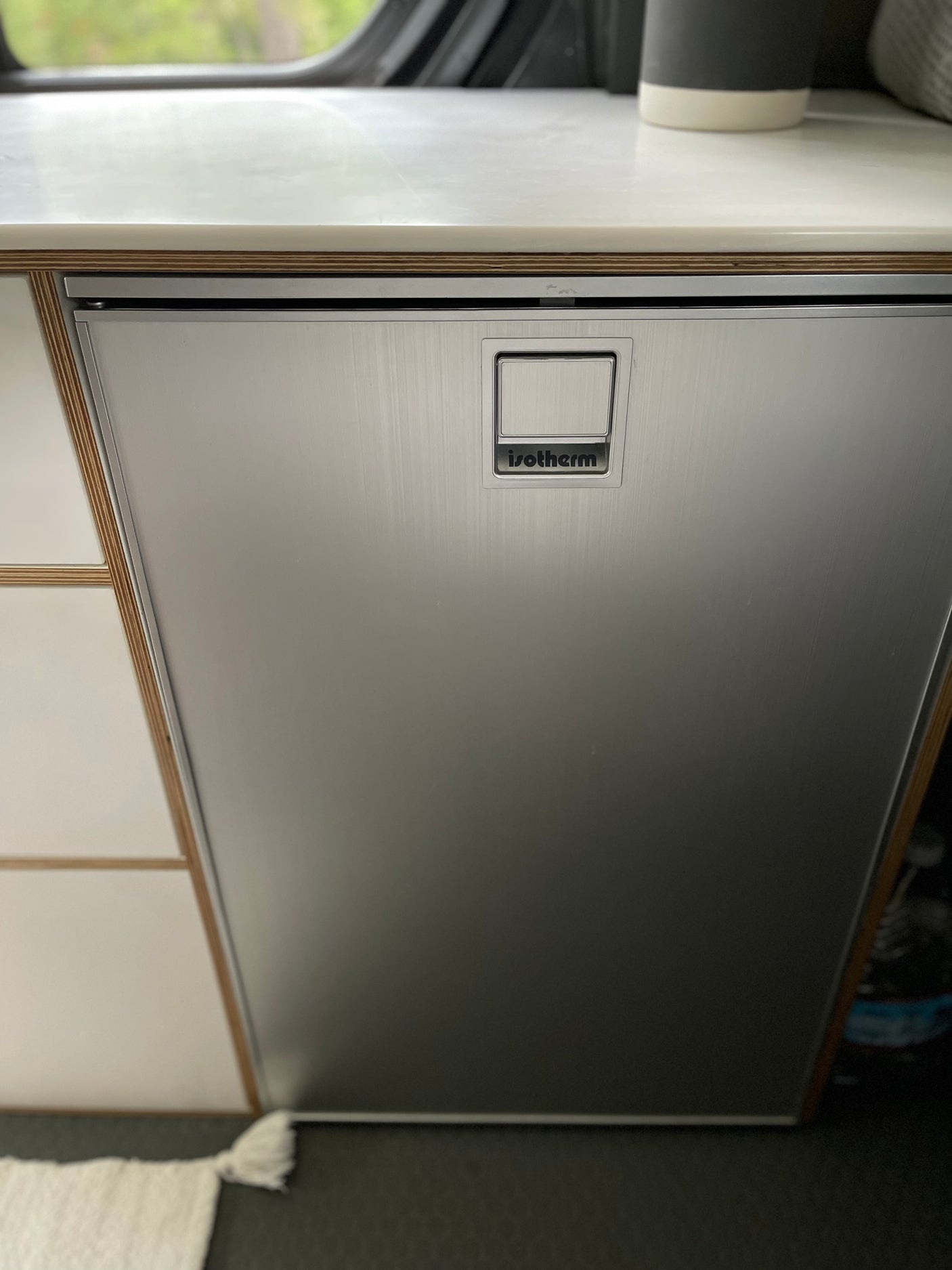 Sleek Isotherm stainless steel refrigerator in an RV rental setup, featuring a wood-layered counter and integrated handle.
