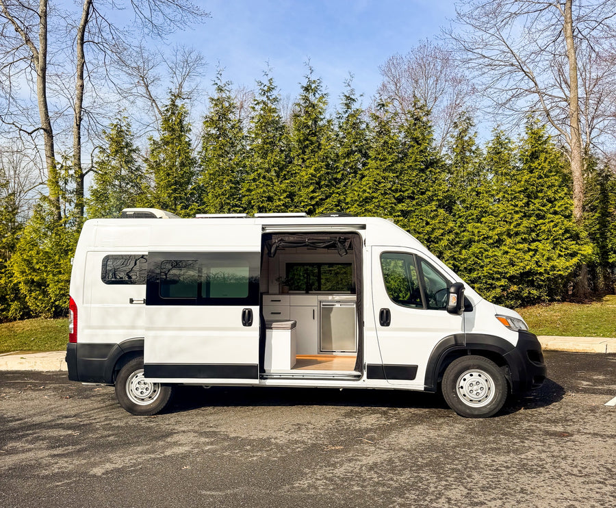 and wood accents.|Smiling man makes pour-over coffee in an RV rental. He brews a fresh cup with a travel mug inside the modern camper van.|RV rental: Modern kitchen with open fridge