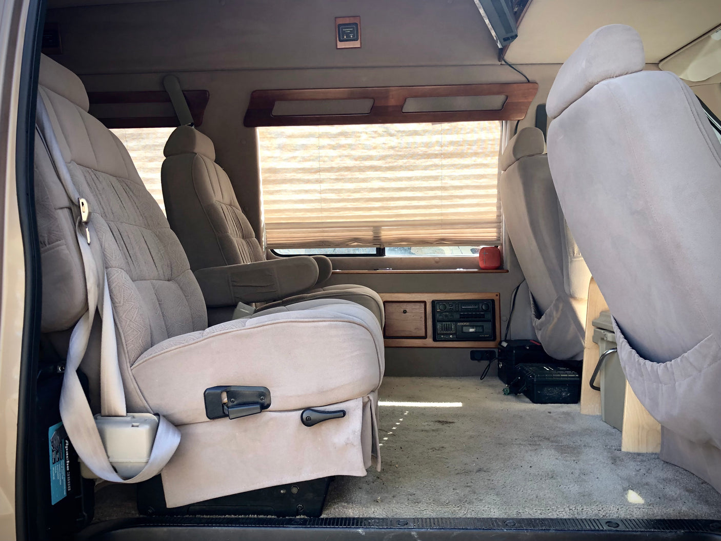 RV rental van interior with tan upholstered seats, pleated window blinds, and a retro cassette player.