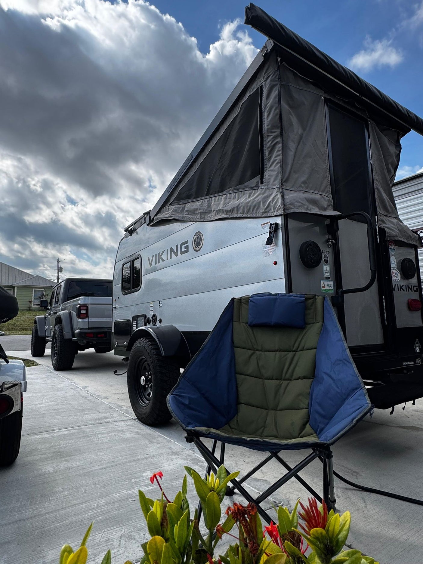 parked next to a Coleman RV and jet ski under a bright sky.|Experience a pop-up RV rental! This grey Viking camper is set up with its tent extended