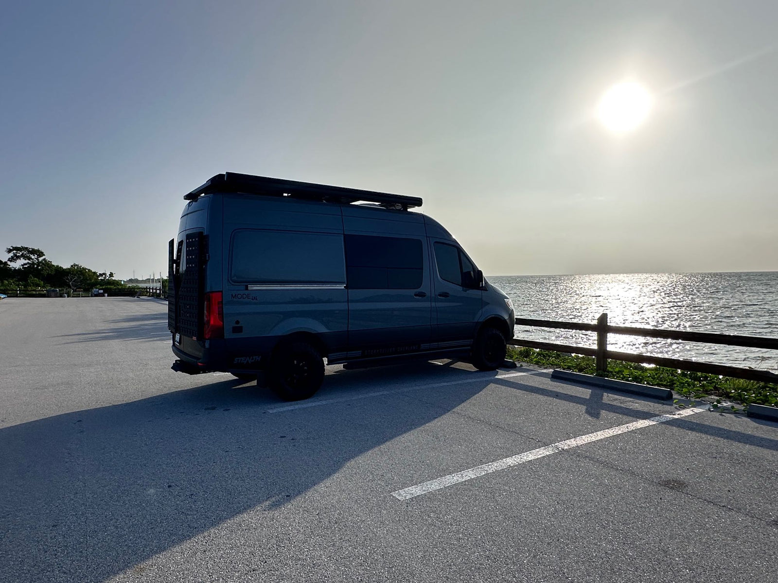This Storyteller Overland camper van by the water, ideal for an rv rental adventure. Sun glints on the waves.