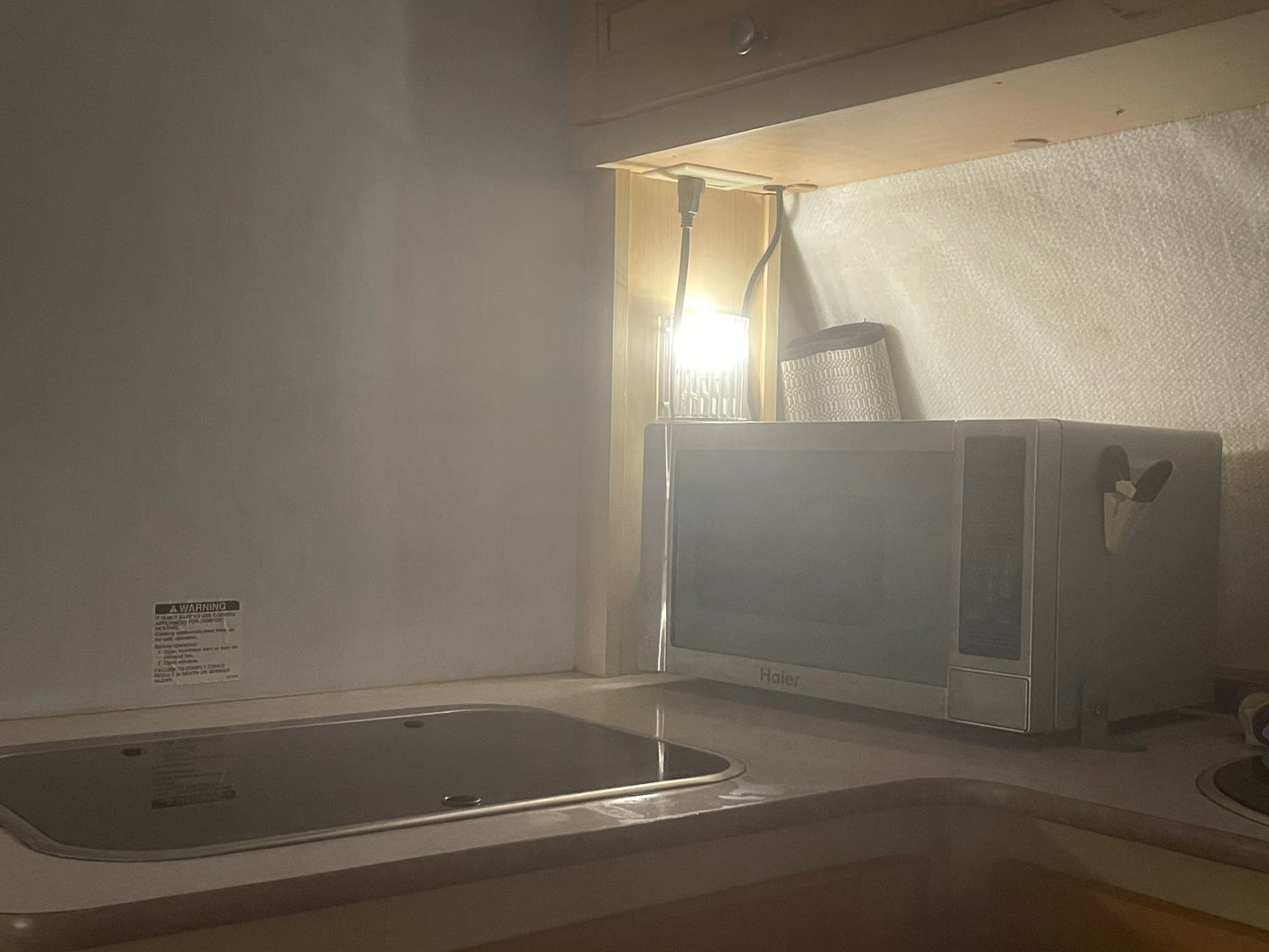 An RV rental galley features a compact kitchen with a flush cooktop/sink cover, a Haier microwave, and under-cabinet lighting.
