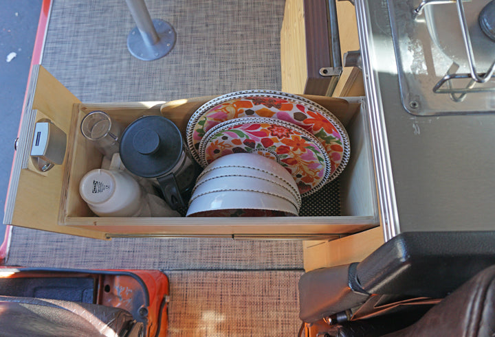 RV rental kitchen drawer open, revealing colorful plates, bowls, coffee press, and a handy USB charger for compact living.