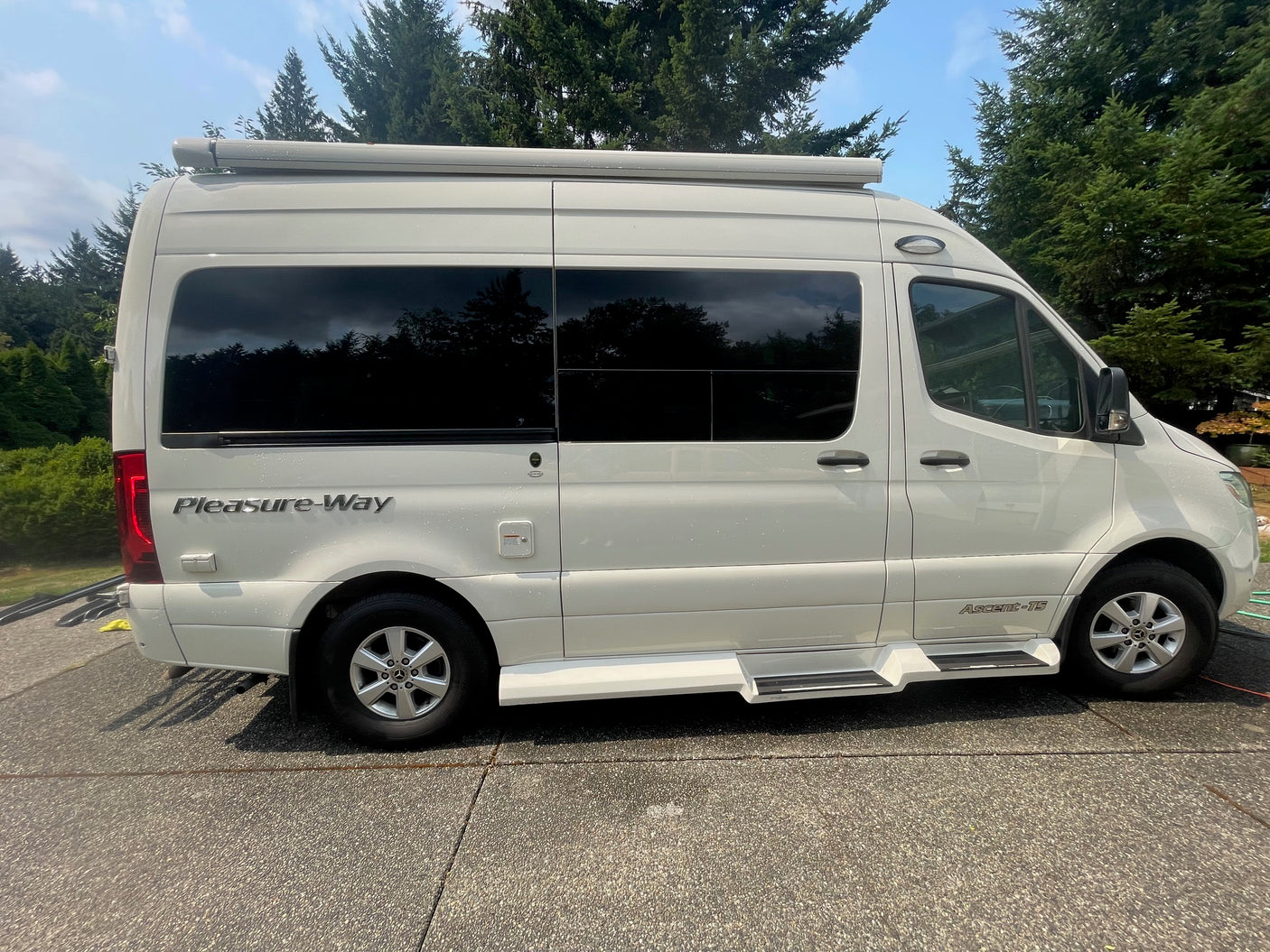 Side view of a white Pleasure-Way Ascent-TS RV rental with tinted windows, parked on a sunny day.