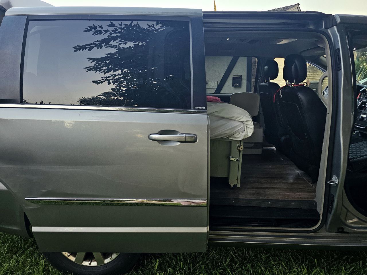 A grey minivan converted into a camper, showcasing a bed and wood flooring inside. Ideal for an rv rental.