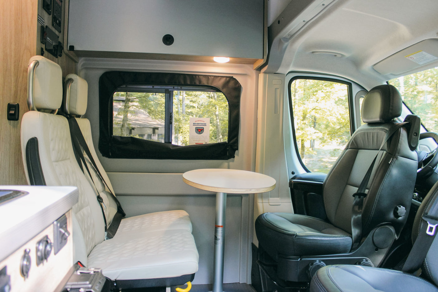 Inside a modern rv rental: bright camper van interior with passenger seating, a small table, and a scenic window view.