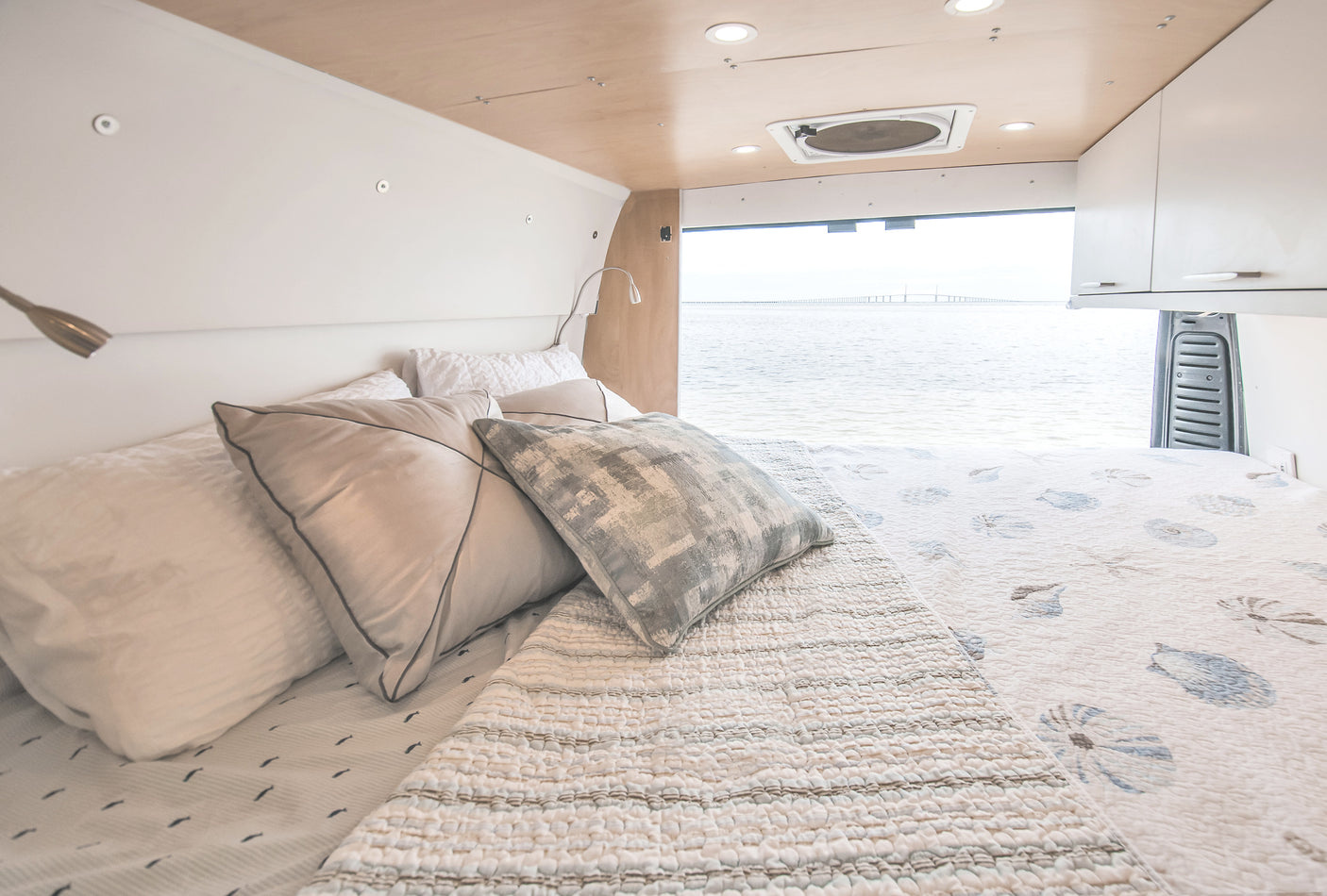 RV rental: Interior of a bright van bedroom with a comfortable bed and panoramic water view, including a bridge.