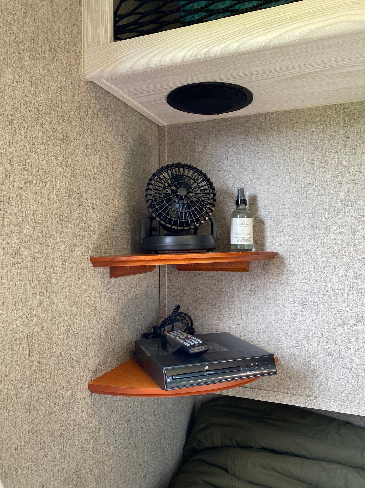 Corner of an RV rental: built-in shelves with a fan, room spray, and DVD player. Speaker overhead for entertainment.