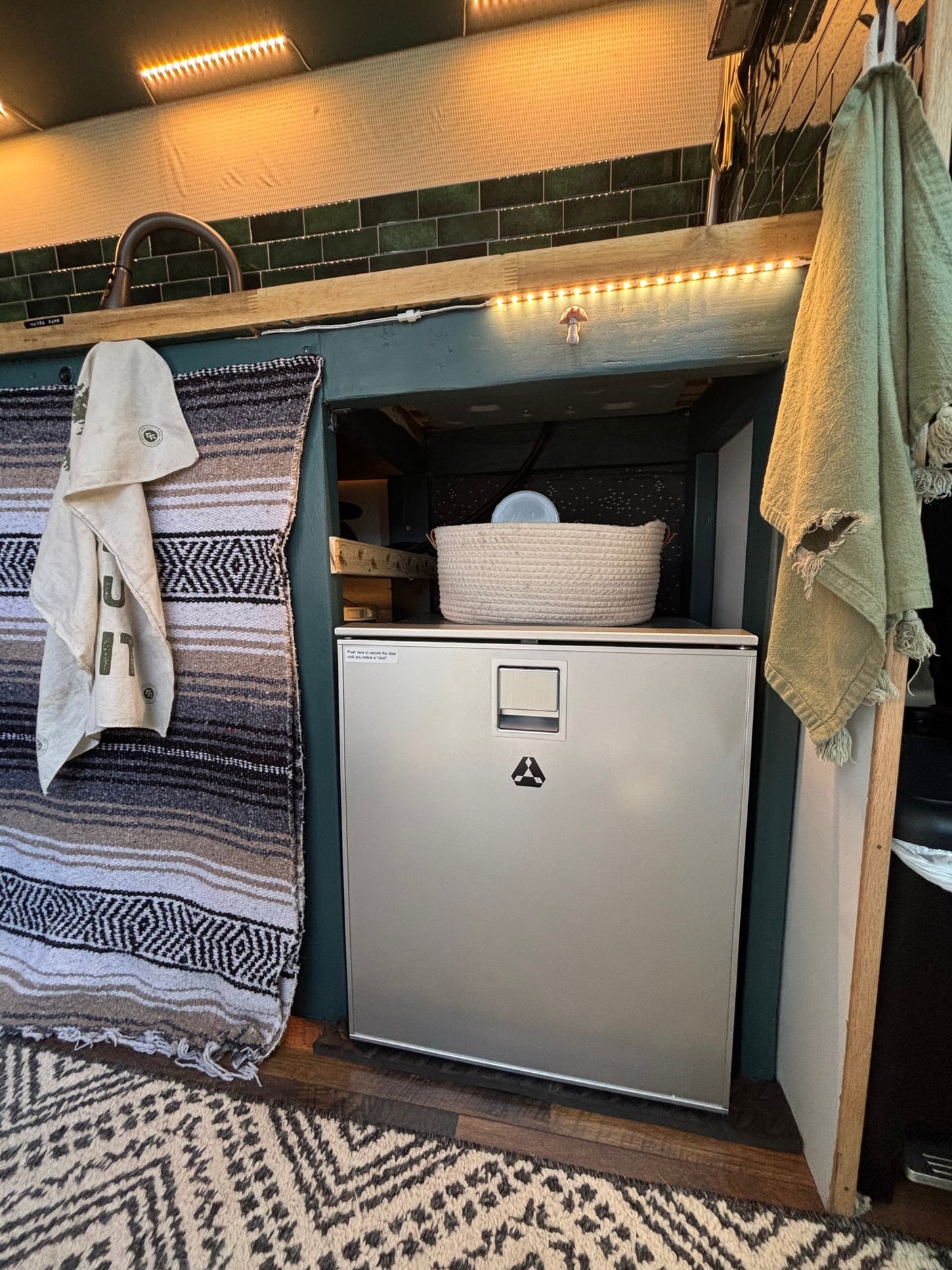 This RV rental showcases a cozy, compact kitchen with a fridge, sink, tiled backsplash, and warm lighting.
