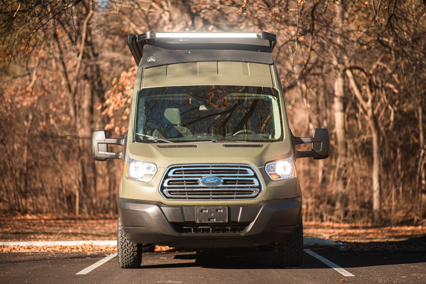 and forest graphics for adventure.|An olive green Ford Transit camper van with custom tree graphics