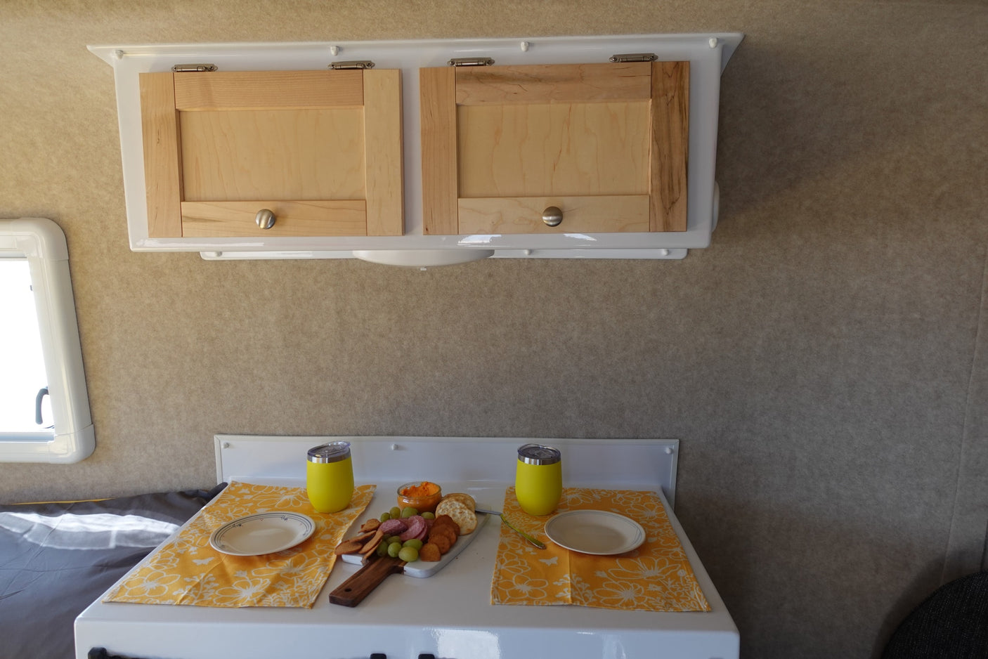 Cozy RV rental interior with light wood cabinets above a dining setup featuring a charcuterie board with snacks and drinks.