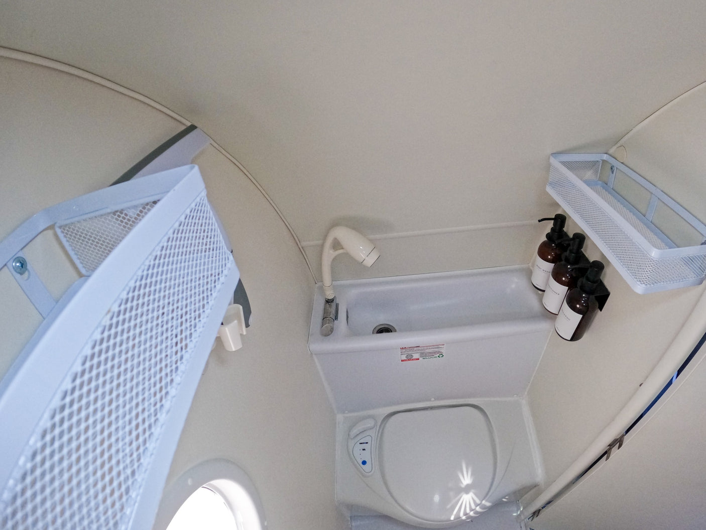 Compact RV rental bathroom: features a toilet, sink with shower sprayer, and wall-mounted baskets for soap and shampoo.