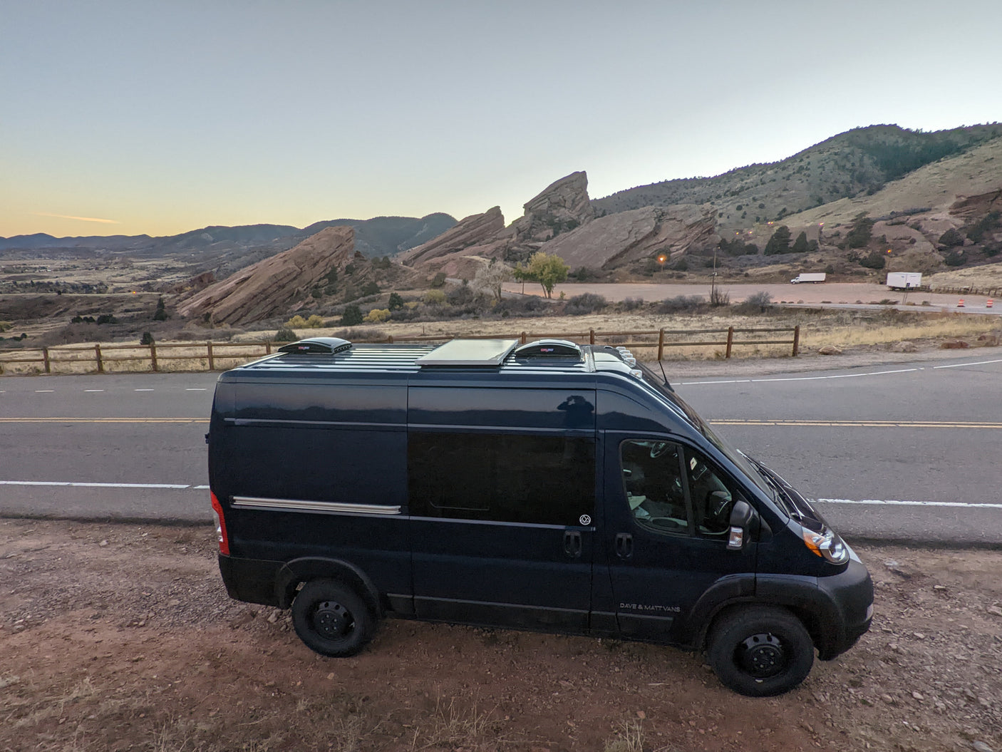Black camper van parked by scenic red rock formations at dusk, a perfect RV rental for outdoor adventures.