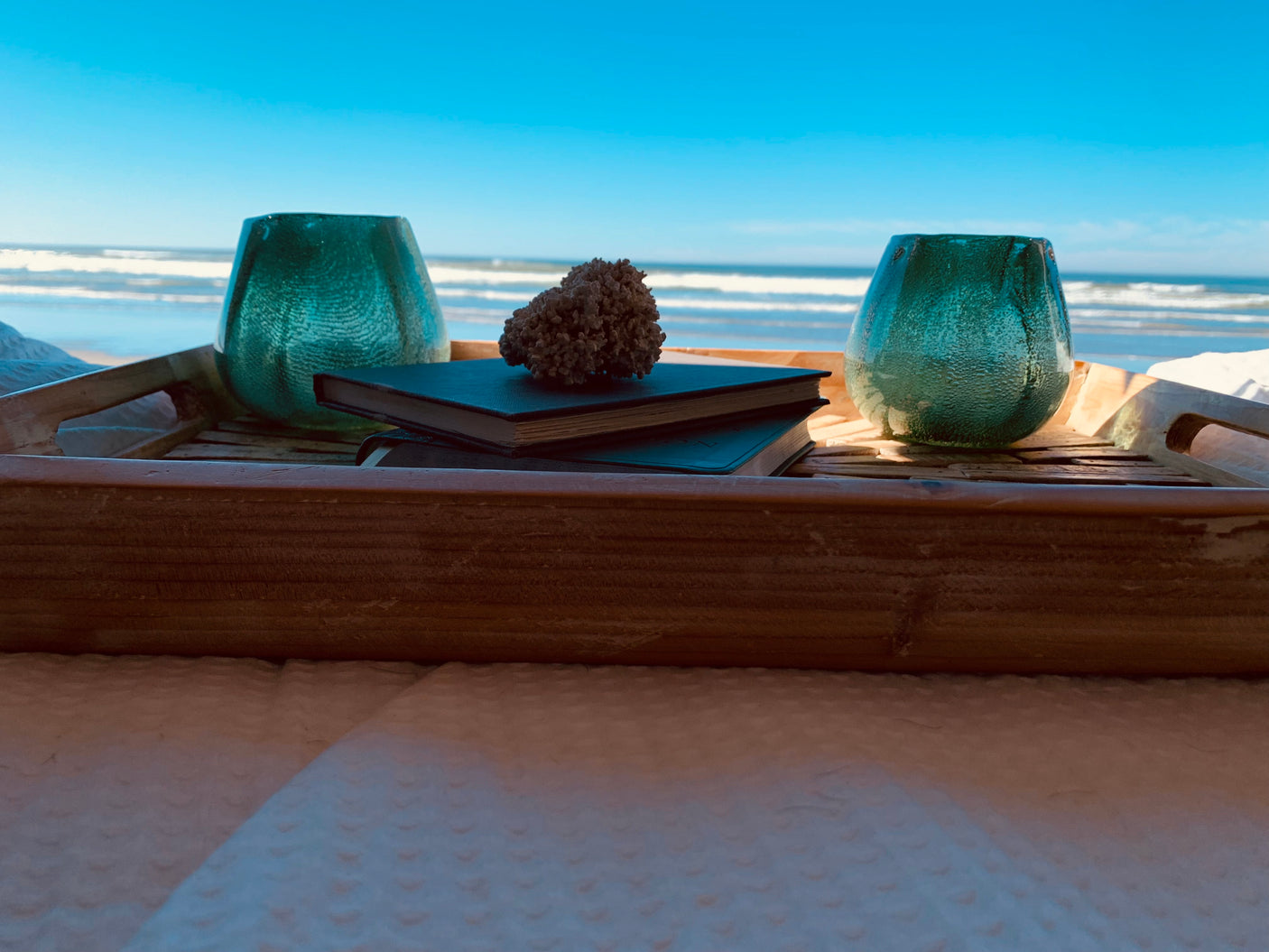 RV rental comfort: A wooden tray with books, teal glass, & coral overlooks the tranquil ocean, perfect for a peaceful retreat.