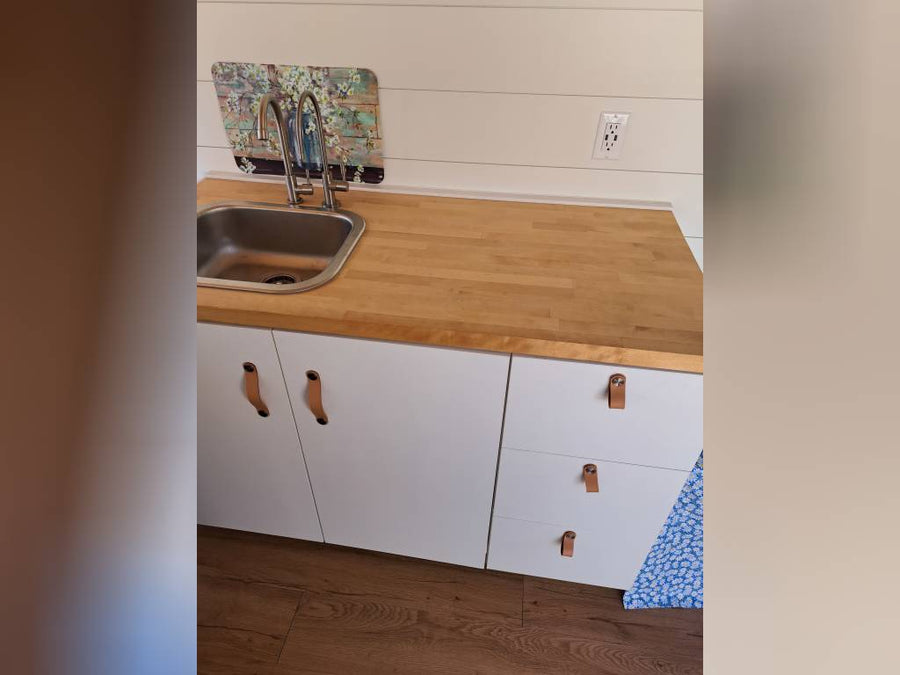 and compact fridge.|Open side of a white camper van shows its custom interior with kitchen and seating