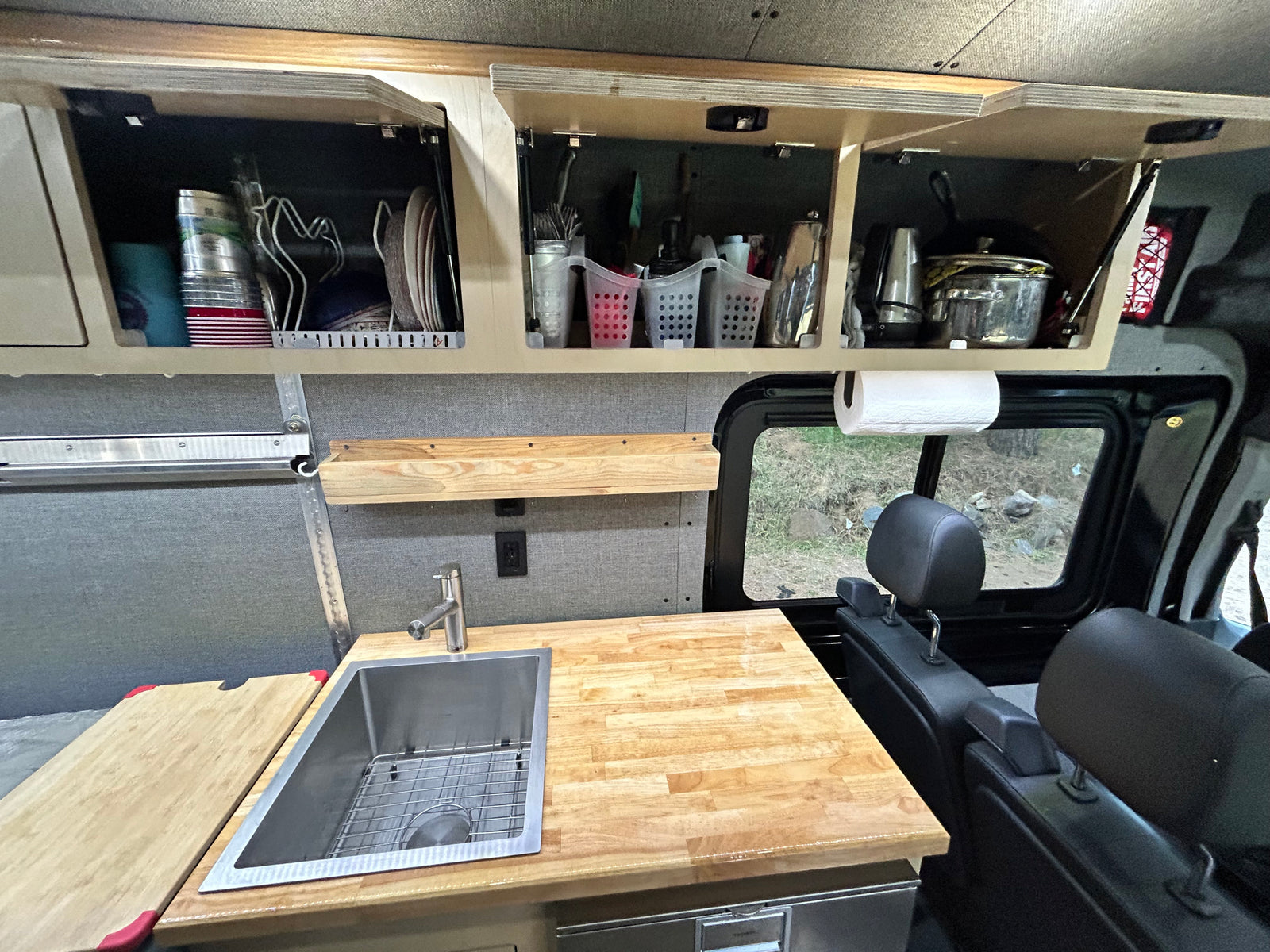 Compact RV rental kitchen with butcher block counter, sink, storage, and paper towel holder, perfect for on-the-go meals.