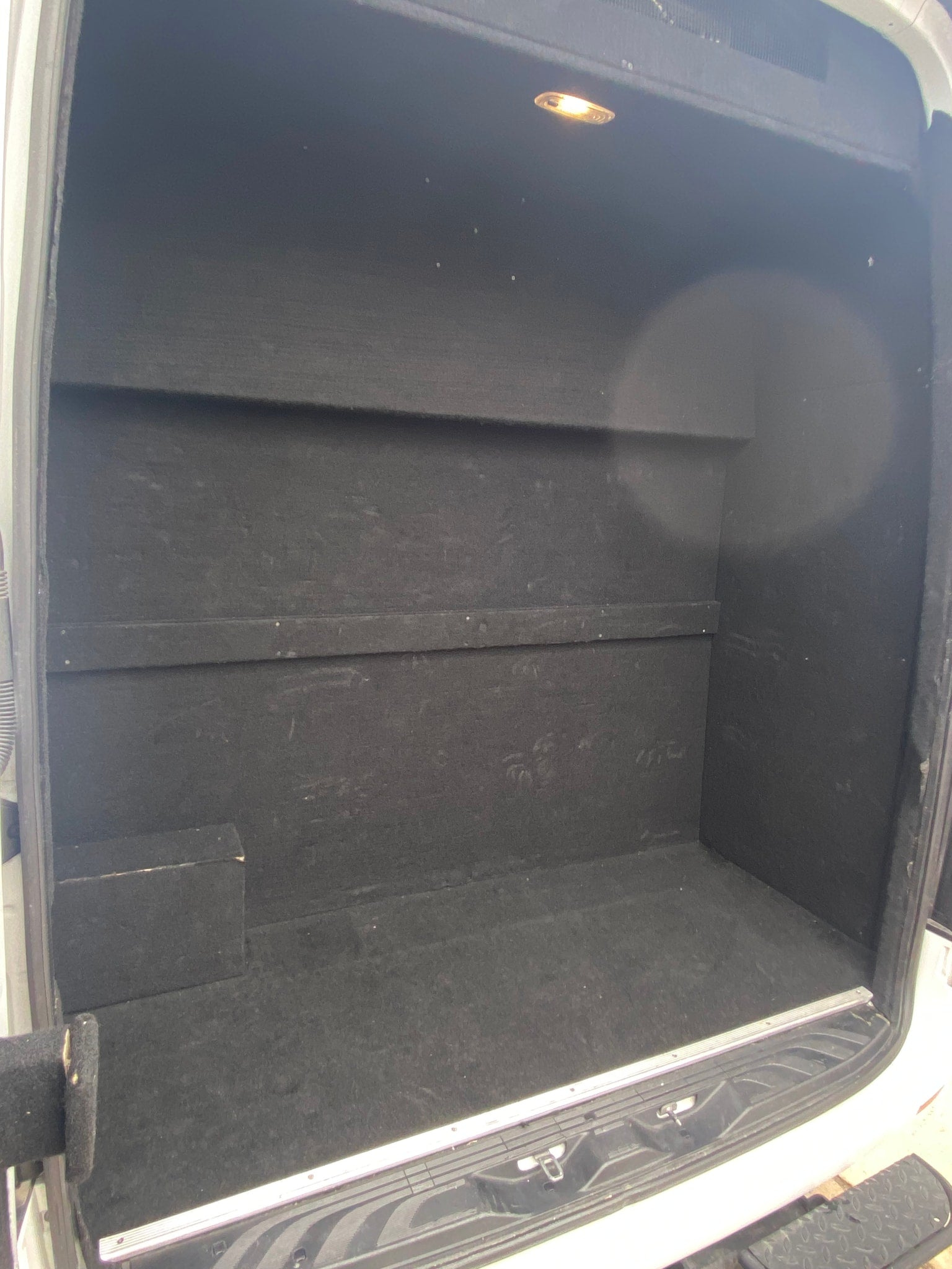 Inside a custom-built RV rental cargo van, featuring a black-lined storage area with built-in shelves and an overhead light.