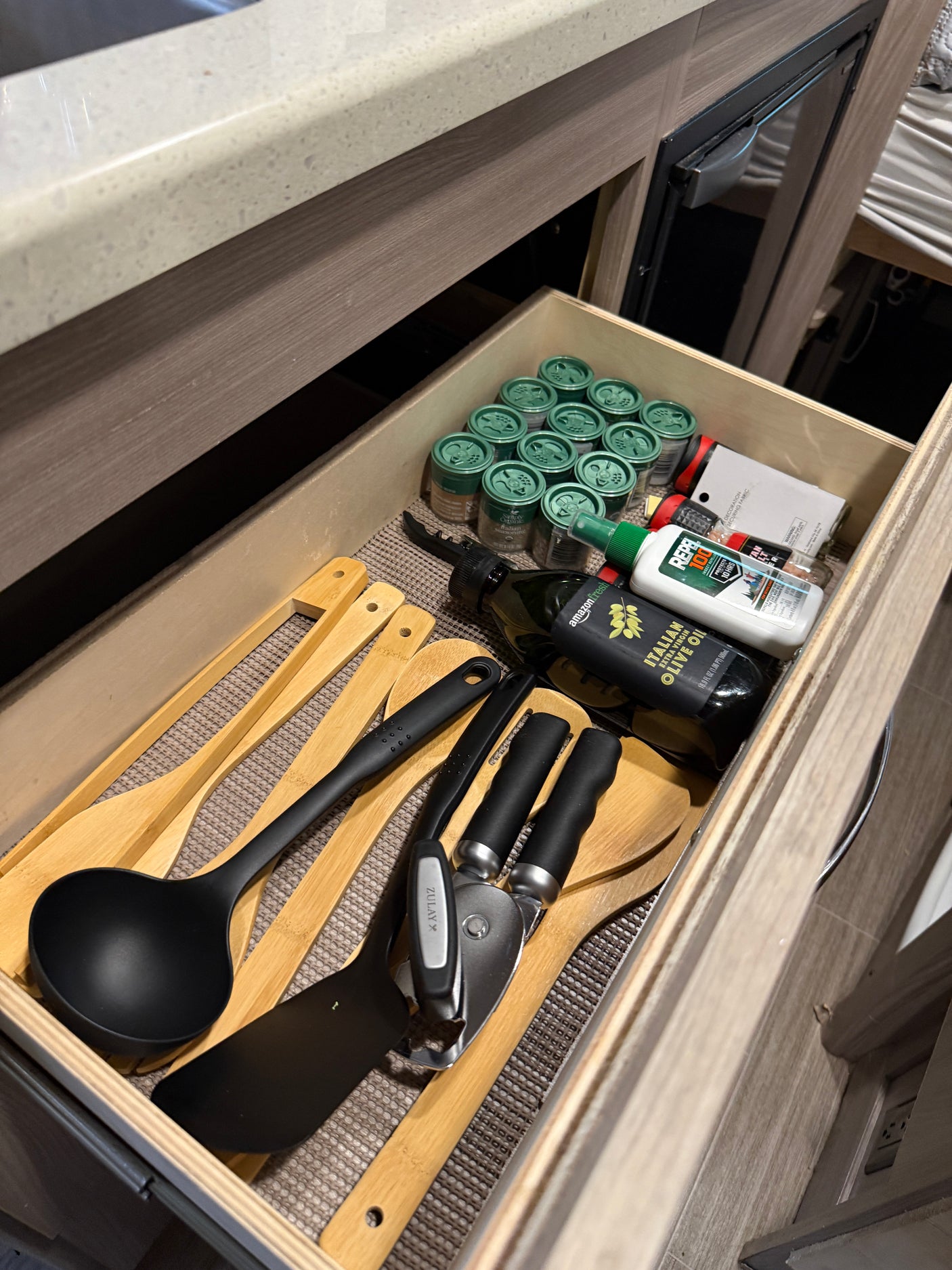 This RV rental kitchen drawer holds cooking utensils, spices, olive oil, and insect repellent, neatly organized for travel.