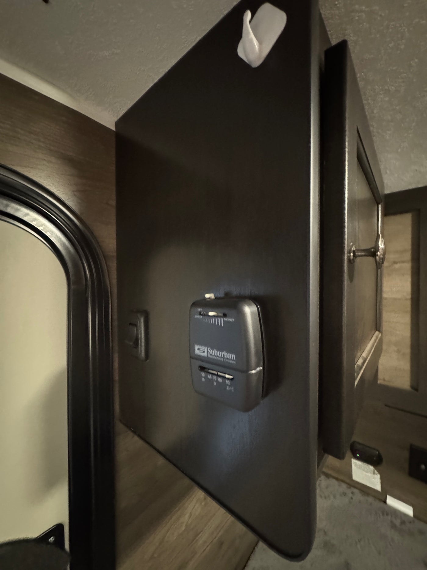 RV rental: Suburban thermostat on a dark panel with light switch and storage cabinet, featuring a white wall hook above. — photo 7