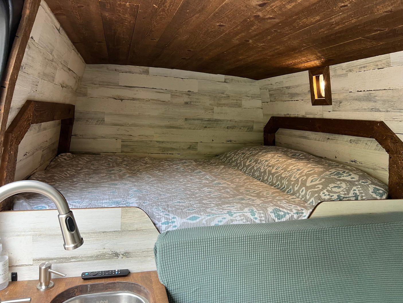 Step inside this cozy rv rental featuring a comfortable bed, stylish wood paneling, and a compact sink area.
