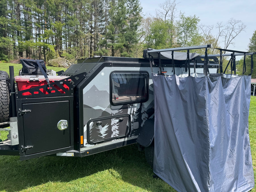 Compact off-road rv rental, gray with mountain graphics, features an attached outdoor privacy screen, ideal for camping.