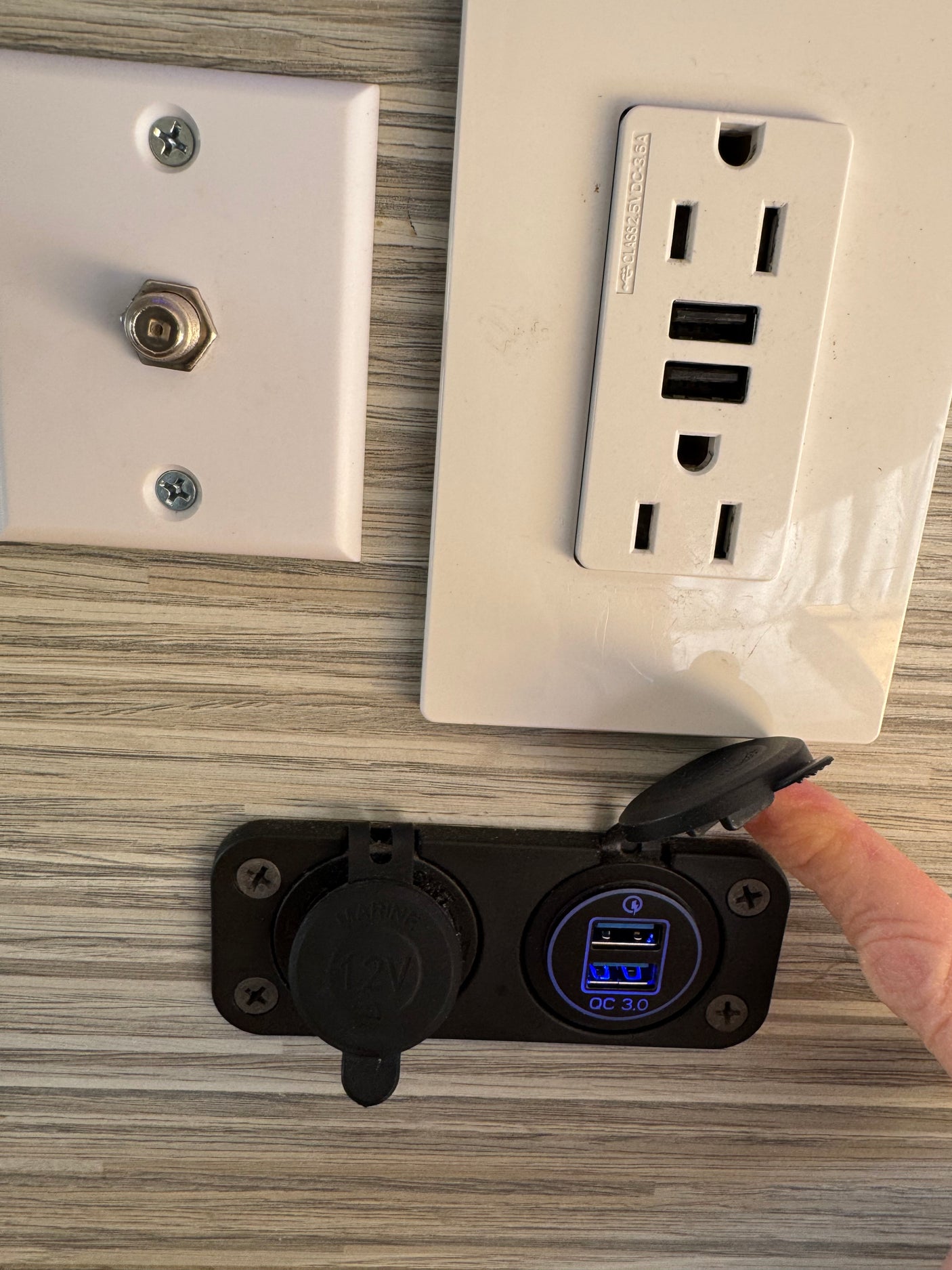 RV rental tech: AC, USB, 12V, & coax outlets on a wood-grain wall. Blue illuminated QC 3.0 USBs ready for charging.