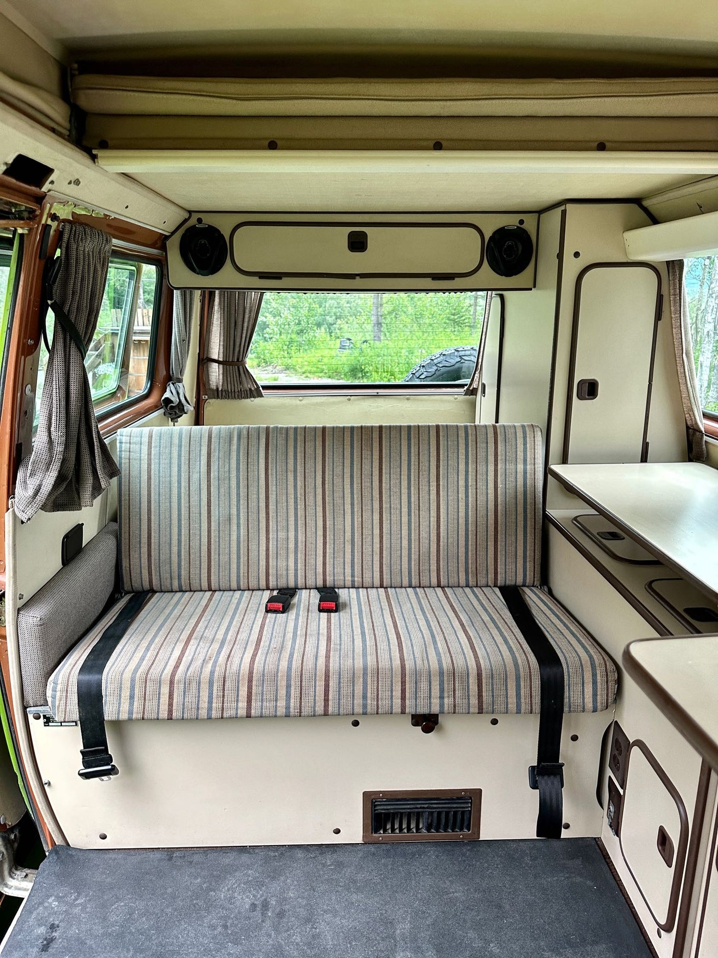 Inside a retro camper van with striped seats, pop-top bed, and compact kitchen. Ideal for an rv rental getaway.