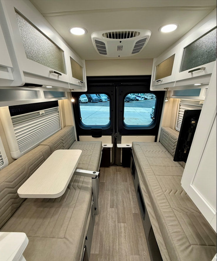 This rv rental features a cozy interior with dual bench seating that converts to beds, a table, and overhead storage.