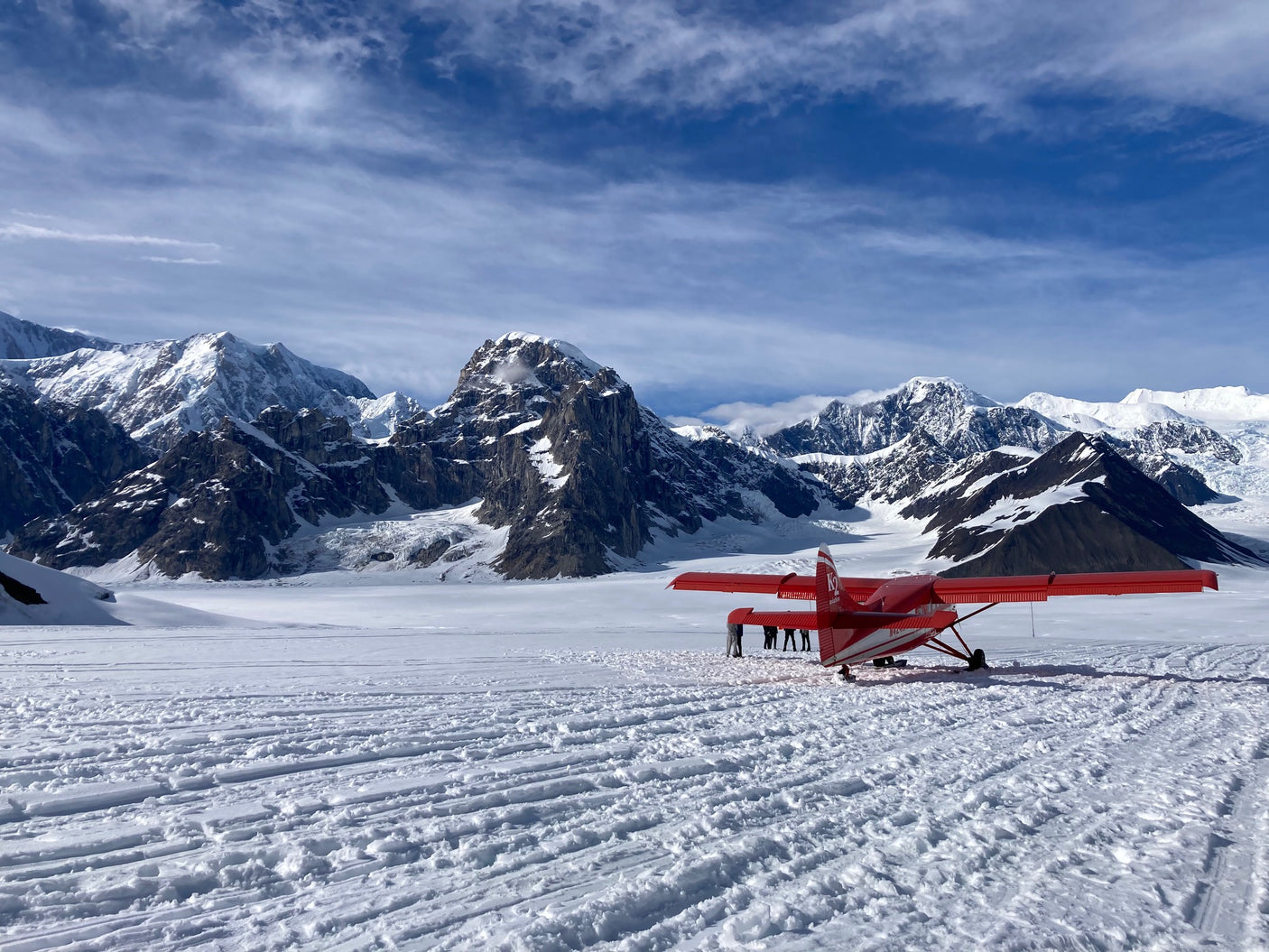 Stunning glacier landing by a red ski plane amidst towering snow mountains. An epic adventure, complementing your RV rental exploration.