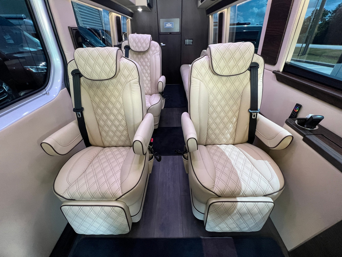 Luxury RV rental interior: Four cream-colored, diamond-quilted leather captain's chairs, wood floor, and modern controls. — photo 4