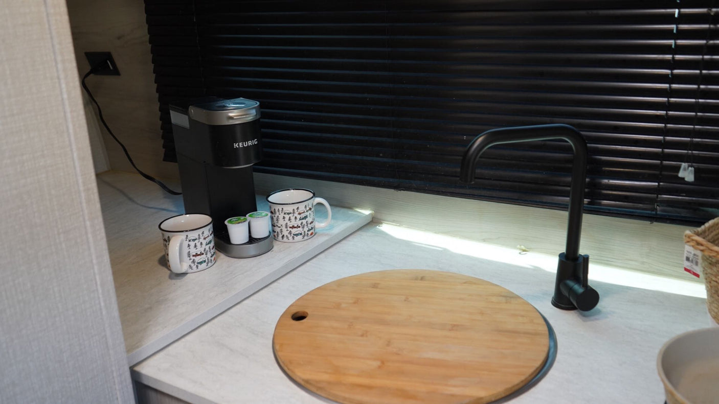 Enjoy amenities like a Keurig coffee maker, mugs, and a modern black faucet on this bright RV rental kitchen counter.
