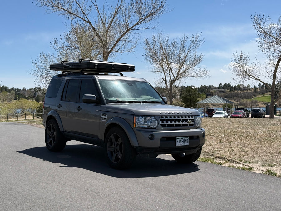 Grey Land Rover Discovery with an RV rental-ready roof-top tent, parked by a lake, perfect for outdoor exploration.