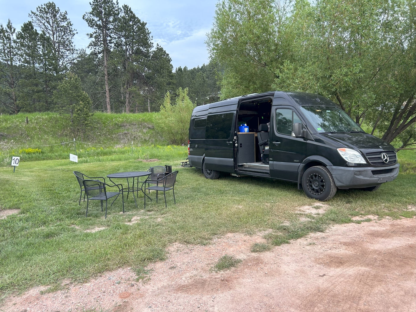 is parked on a sunlit grassy area near dense foliage.|Explore in this black Mercedes Sprinter van — photo 4