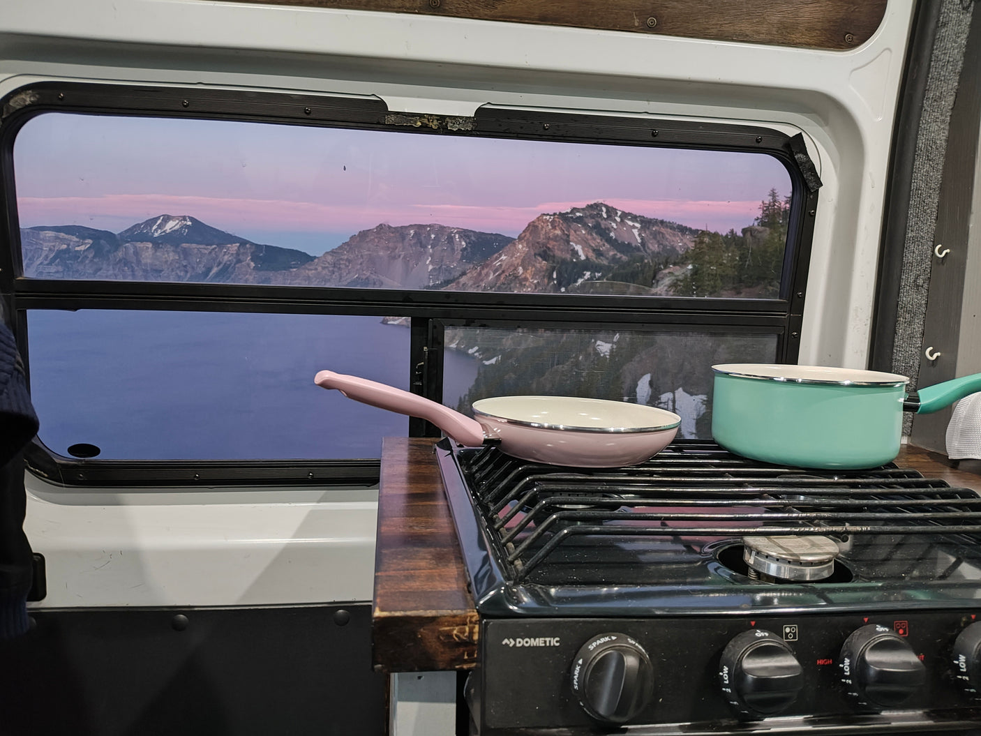 Crater Lake sunset from an rv rental window, featuring a Dometic stovetop with pink and teal cookware for a scenic meal.