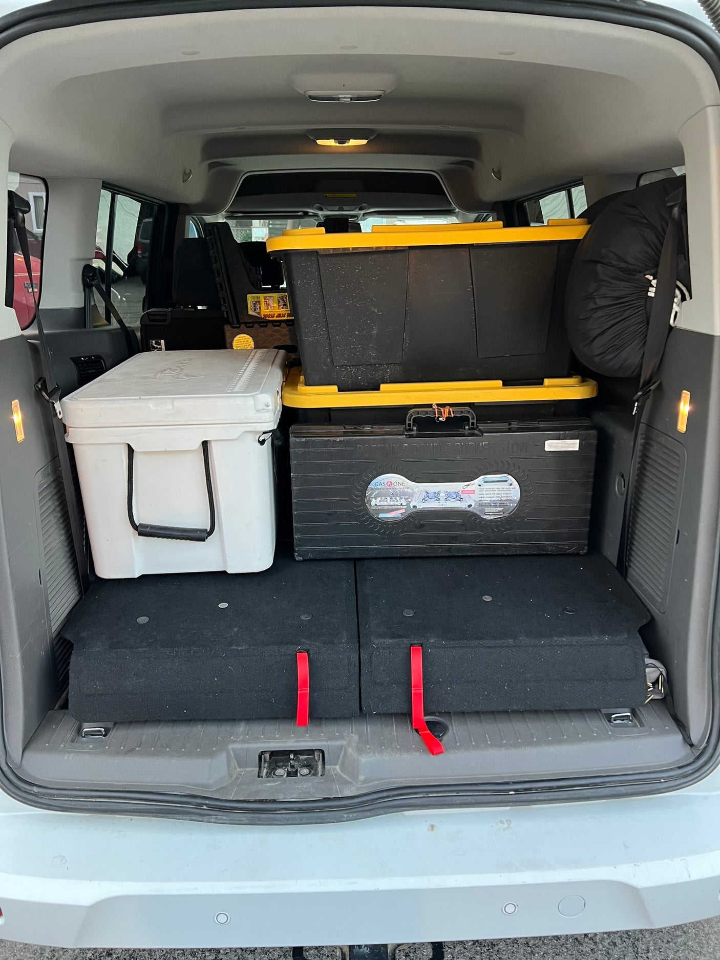 This vehicle's cargo space, perfect for an rv rental, is efficiently packed with a cooler, bins, and stove for a road trip.