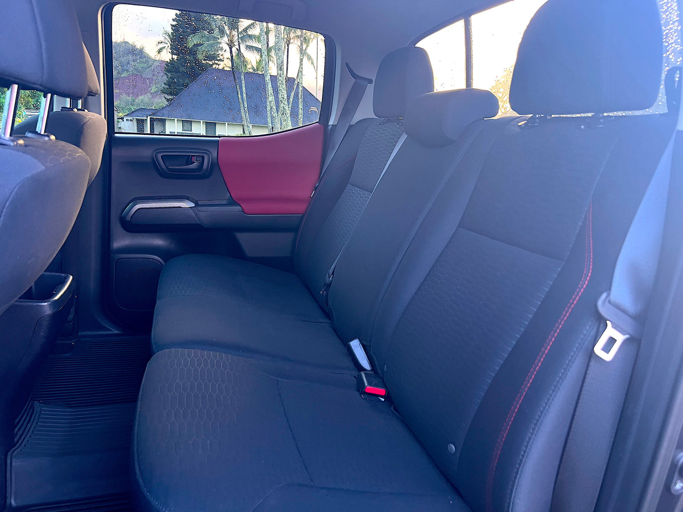 Comfortable rear seats inside a vehicle, ready for your RV rental. Rain-kissed window reveals a tropical landscape.