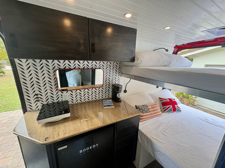 Compact rv rental interior featuring bunk beds, a modern kitchenette, and stylish overhead cabinets, perfect for van life.