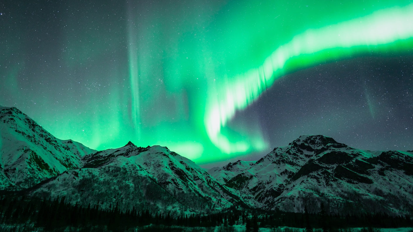 Aurora borealis brilliantly illuminates snow-capped mountains and starry skies, ideal for an RV rental journey.