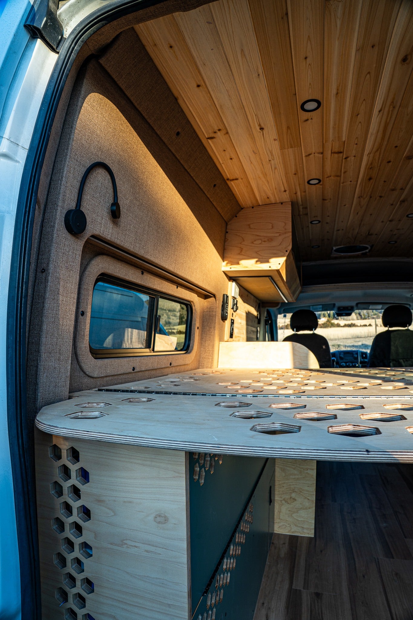 Explore this custom **rv rental** interior. Features a warm wooden ceiling, unique perforated bed platform, and cozy fabric walls.