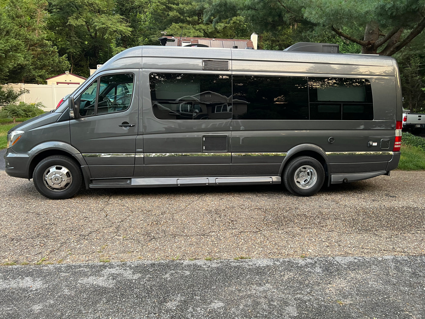 with its awning extended in a sunny parking lot.|Full side view of a dark gray Mercedes-Benz Sprinter RV van
