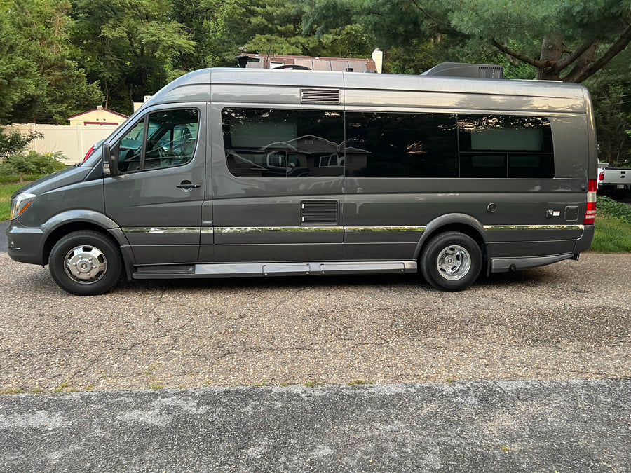 with its awning extended in a sunny parking lot.|Full side view of a dark gray Mercedes-Benz Sprinter RV van