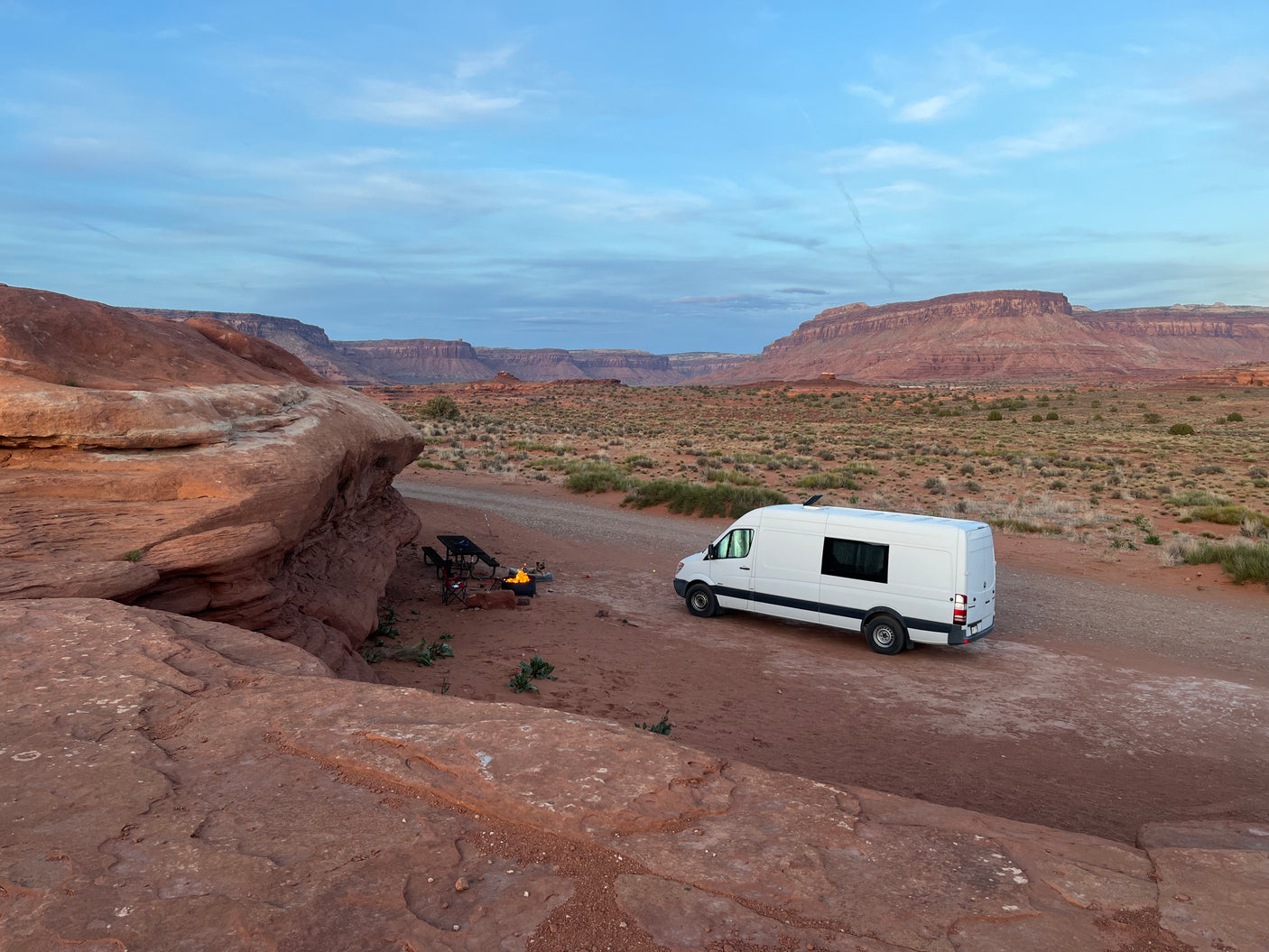 Enjoying the desert! A white RV rental van is set up with a campfire, chairs, and stunning red rock views.