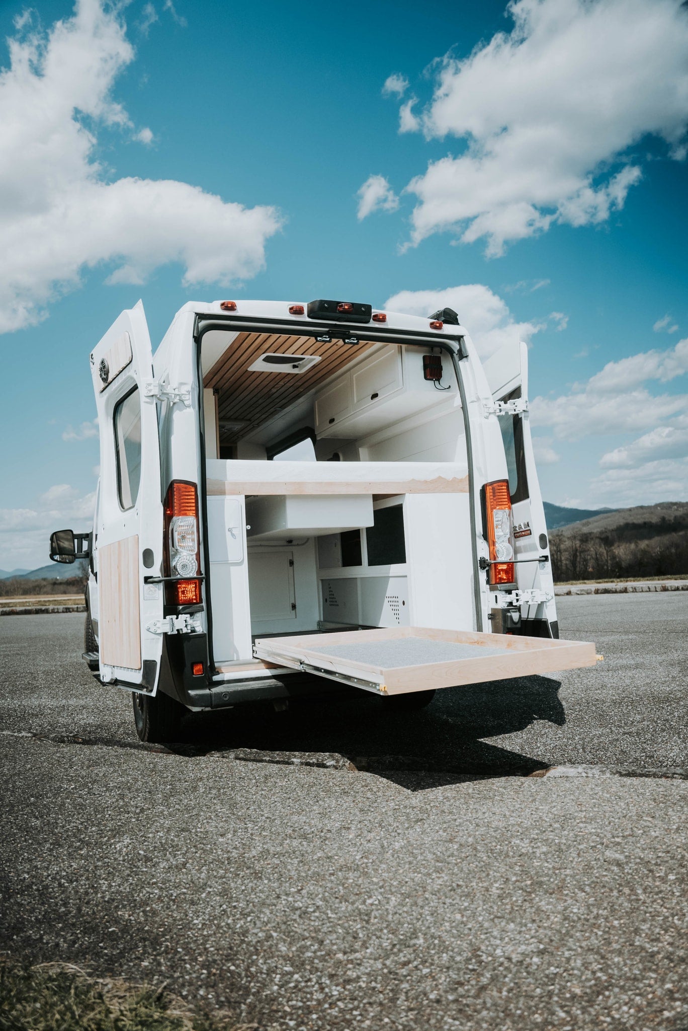 side door open to reveal its interior. Cloudy sky above.|Explore our custom-built RV rental camper van with open rear doors