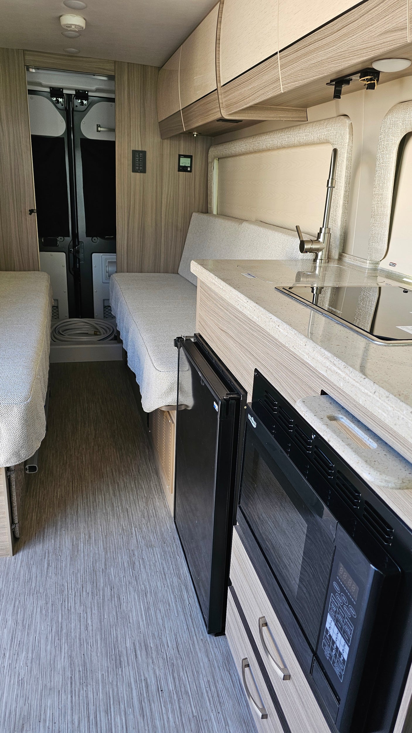 RV rental interior: cozy camper van with kitchen counter, sink, microwave, fridge, and convertible twin beds.