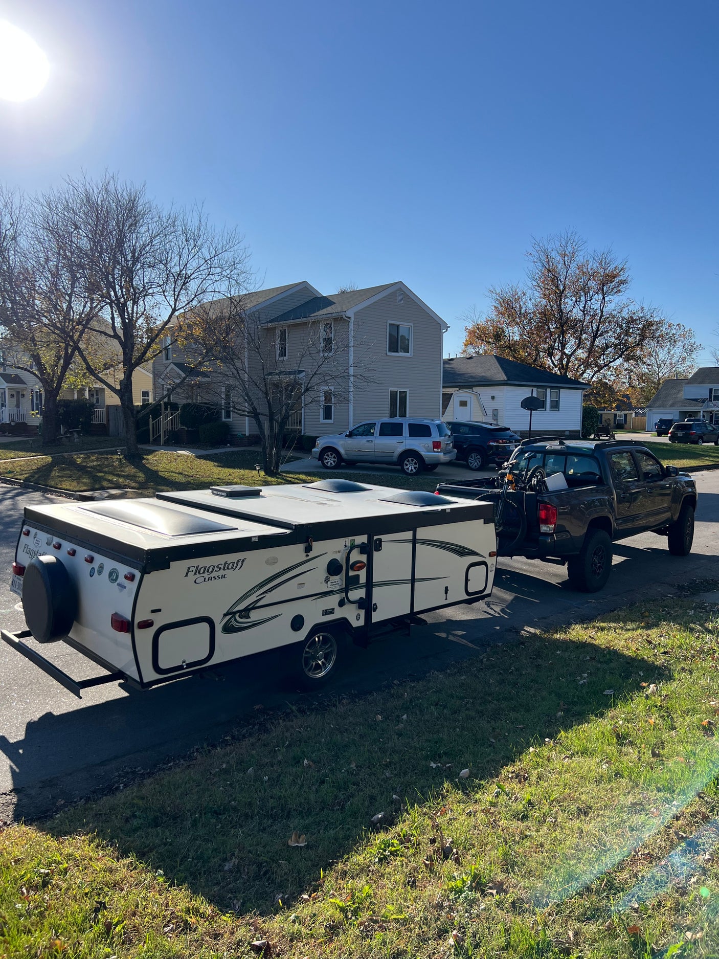 A pop-up camper (Flagstaff Classic) hitched to a pickup truck, ready for an RV rental adventure. Sunny residential street scene.