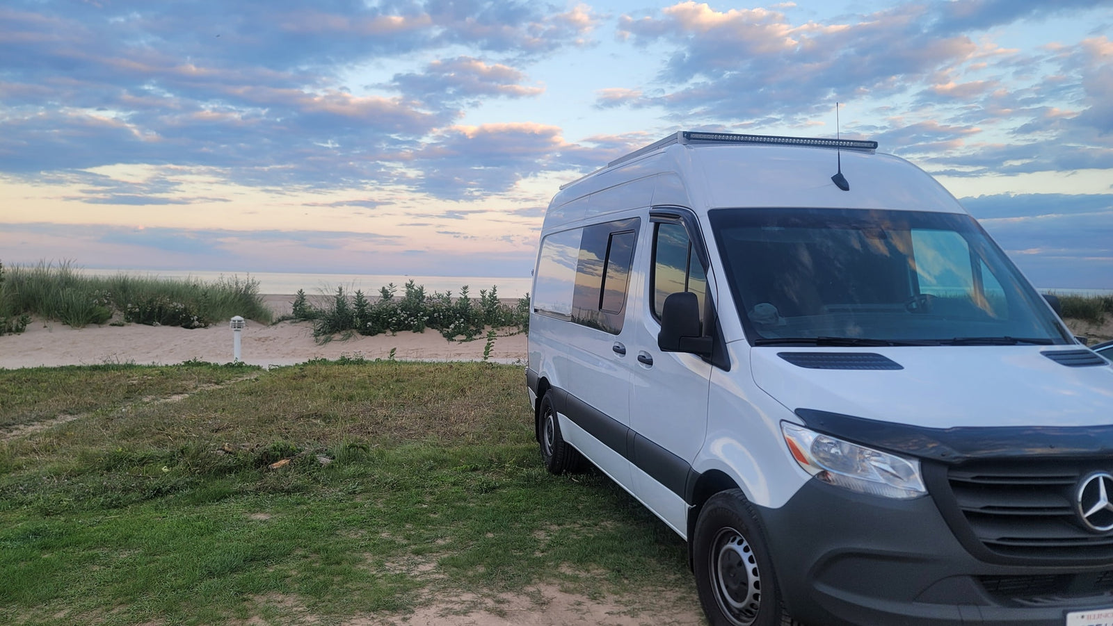 parked by a scenic beach at sunset.|White Mercedes-Benz Sprinter van