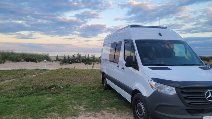parked by a scenic beach at sunset.|White Mercedes-Benz Sprinter van