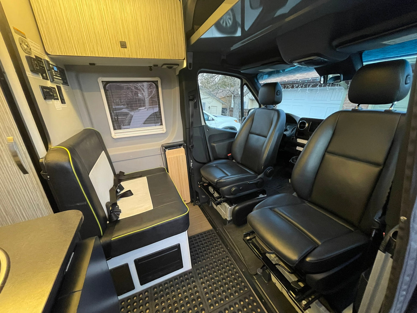 This rv rental shows a compact camper van's interior with black leather front seats, a side bench, controls, and cabinets.